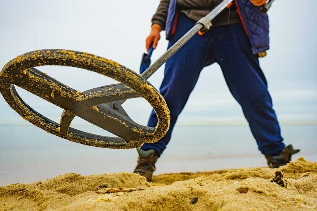 man standing with metal detector in sand