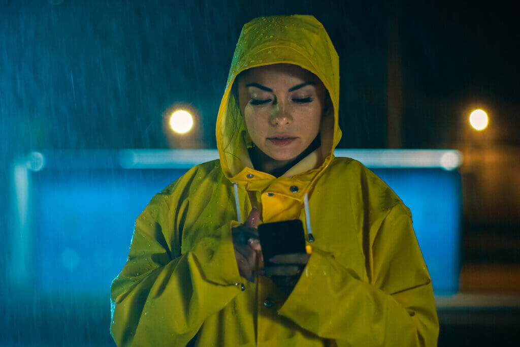 woman in mackintosh uses smartphone in the rain